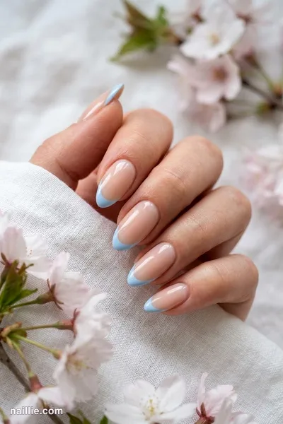 Close-up of almond nails with baby blue French tips over a sheer nude base