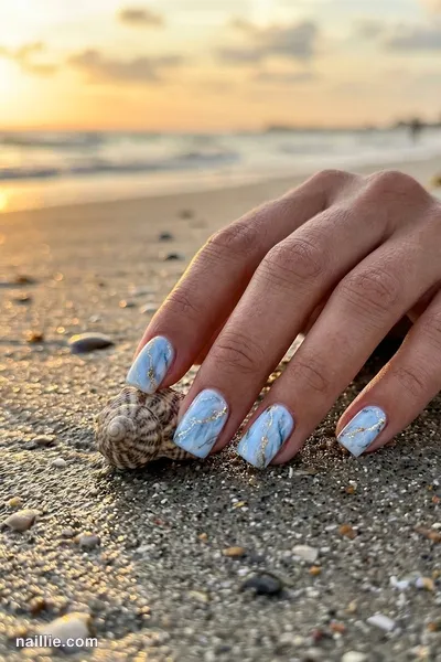 Close-up of short square nails with baby blue marble swirls with gold veins
