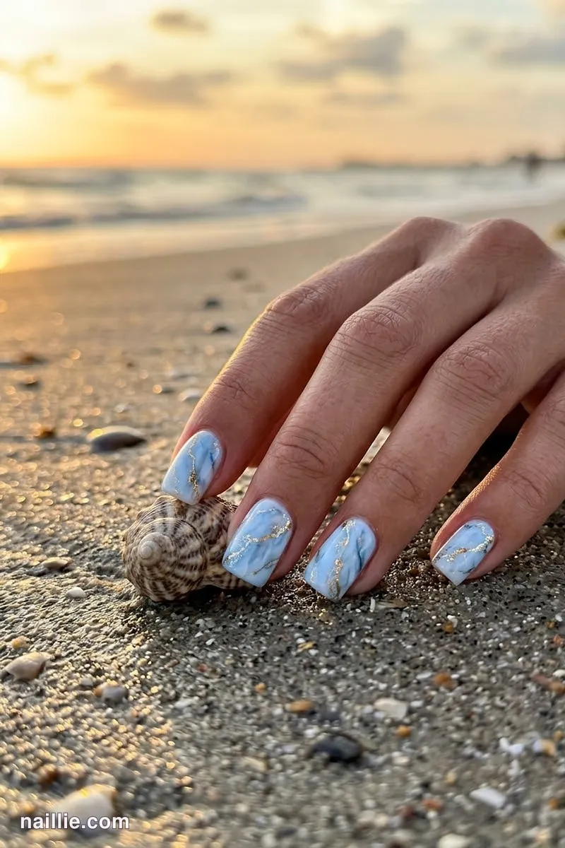 Close-up of short square nails with baby blue marble swirls with gold veins