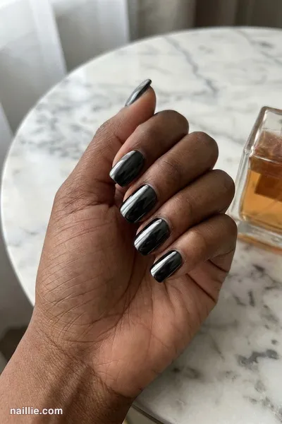 Close-up of short square nails with black polish and a mirror-like chrome finish