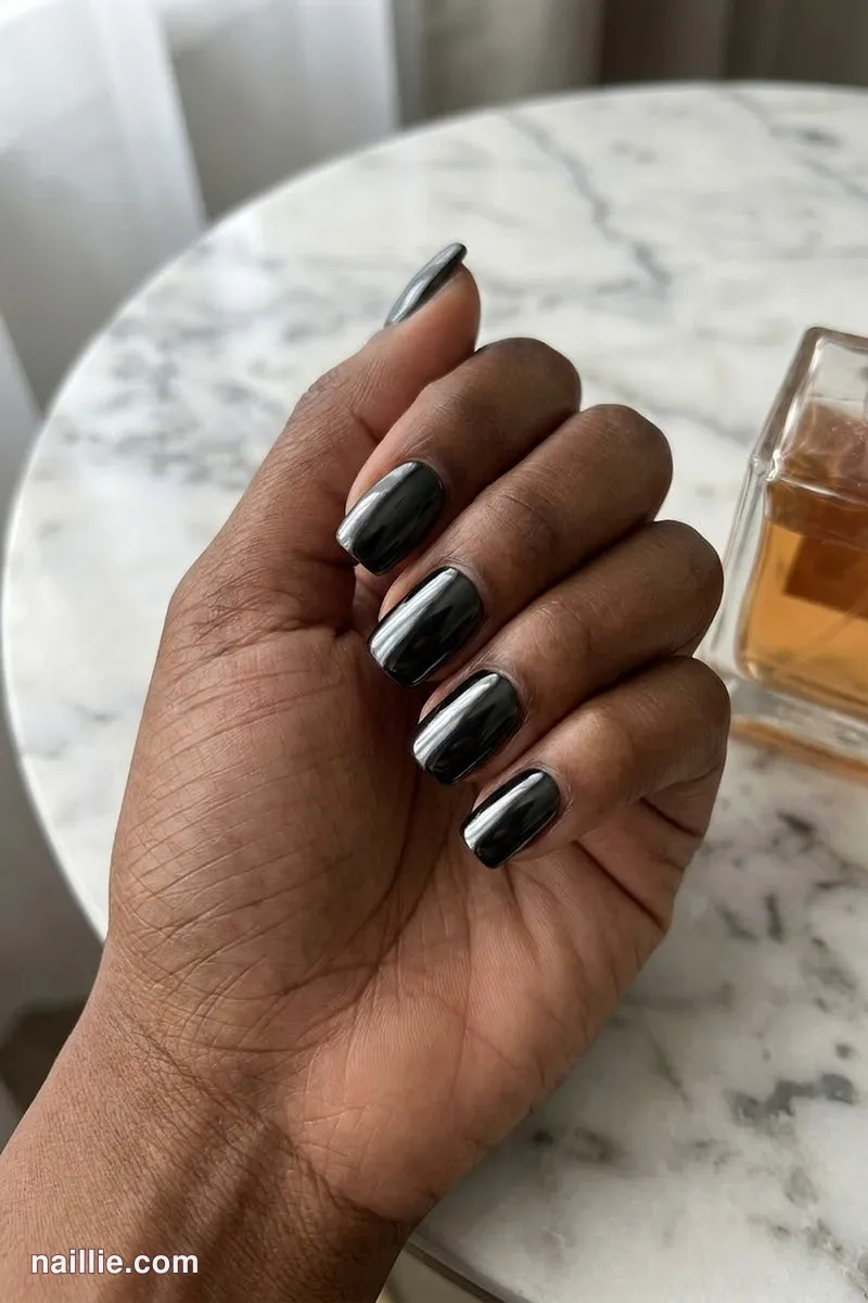 Close-up of short square nails with black polish and a mirror-like chrome finish