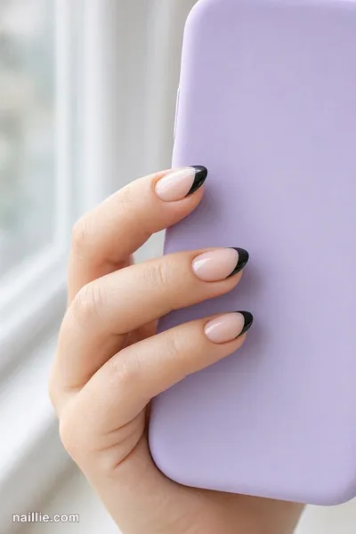 Close-up of almond nails with black French tips over a sheer nude base