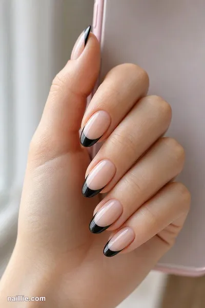 Close-up of almond nails with black French tips over a sheer nude base — look 2