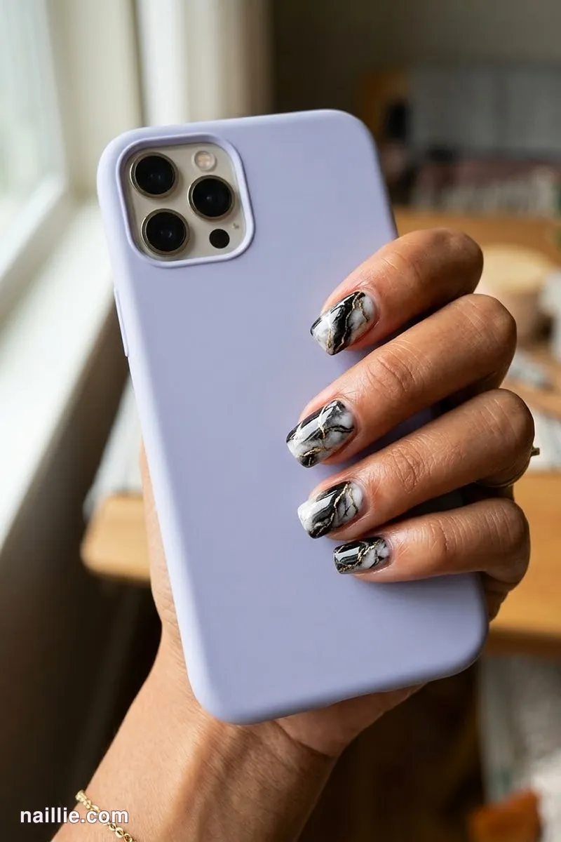 Close-up of short square nails with black marble swirls with gold veins