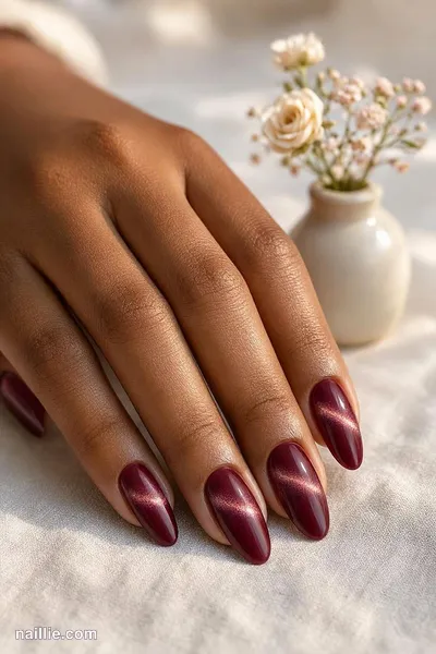 Close-up of almond nails with burgundy polish and a shimmering magnetic cat eye effect