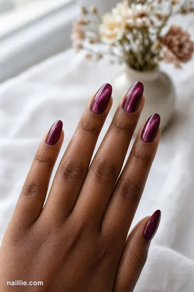 Close-up of almond nails with burgundy polish and a shimmering magnetic cat eye effect — look 2
