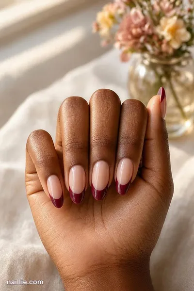 Close-up of almond nails with burgundy French tips over a sheer nude base