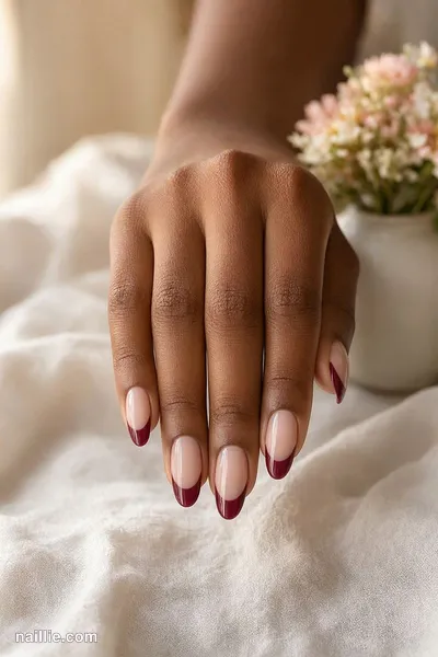 Close-up of almond nails with burgundy French tips over a sheer nude base — look 2