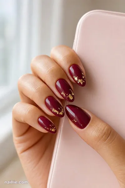 Close-up of almond nails with burgundy polish and delicate gold foil flakes — look 3