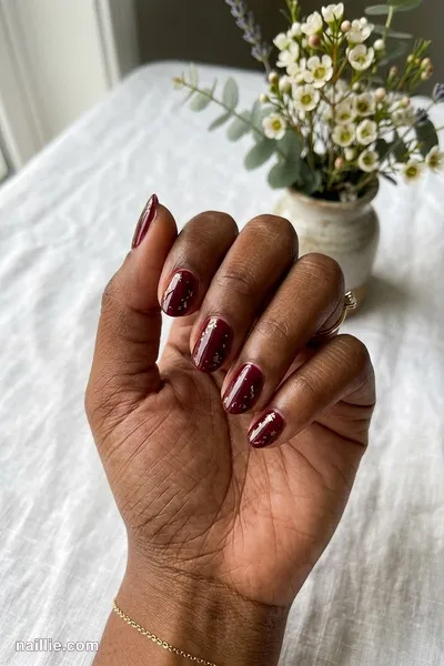 Close-up of short almond nails with burgundy polish and delicate gold foil flakes — look 2
