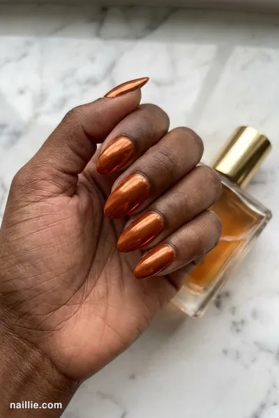 Close-up of almond nails with burnt orange polish and a mirror-like chrome finish — look 2