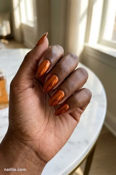 Close-up of almond nails with burnt orange polish and a mirror-like chrome finish — look 3