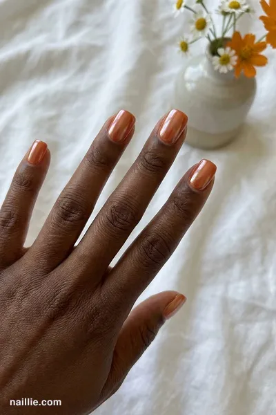 Close-up of short square nails with burnt orange polish and a pearly glazed-donut shimmer