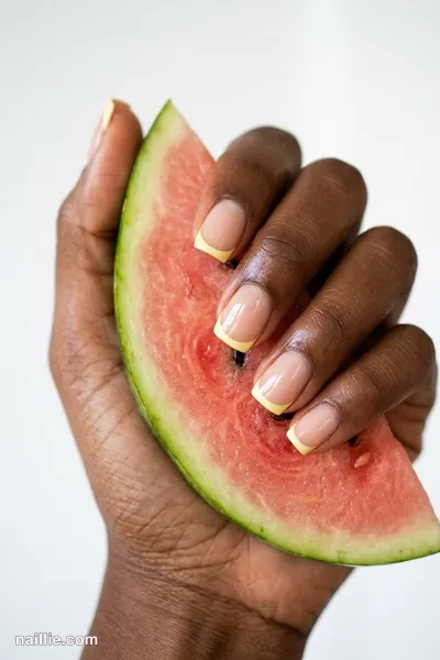 Close-up of short square nails with butter yellow French tips over a sheer nude base