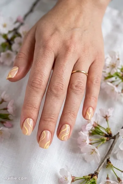 Close-up of short square nails with butter yellow abstract swirls on a nude base — look 2