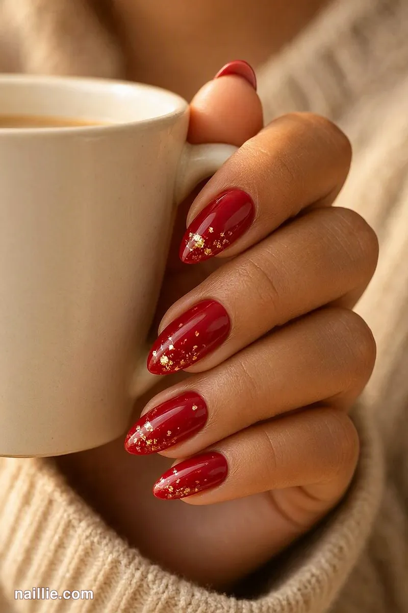 Close-up of almond nails with cherry red polish and delicate gold foil flakes
