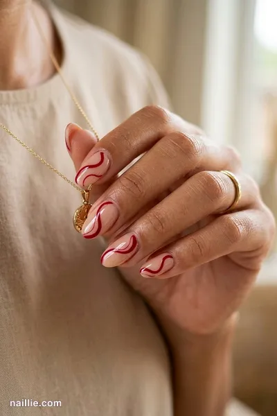 Close-up of oval nails with cherry red abstract swirls on a nude base