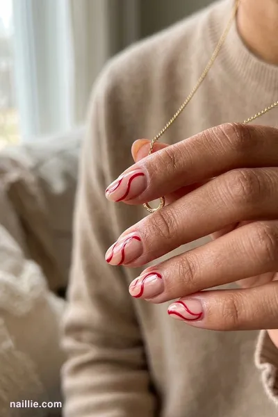 Close-up of oval nails with cherry red abstract swirls on a nude base — look 2