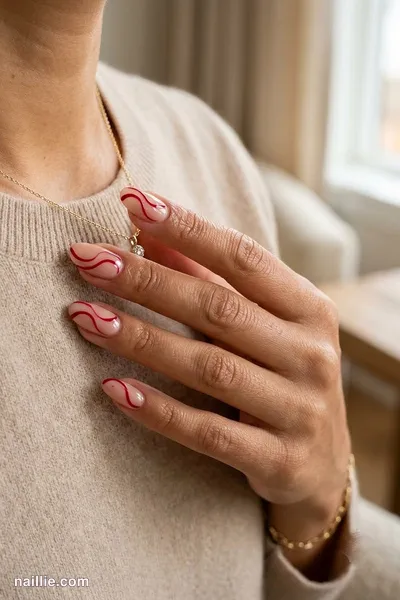 Close-up of oval nails with cherry red abstract swirls on a nude base — look 3