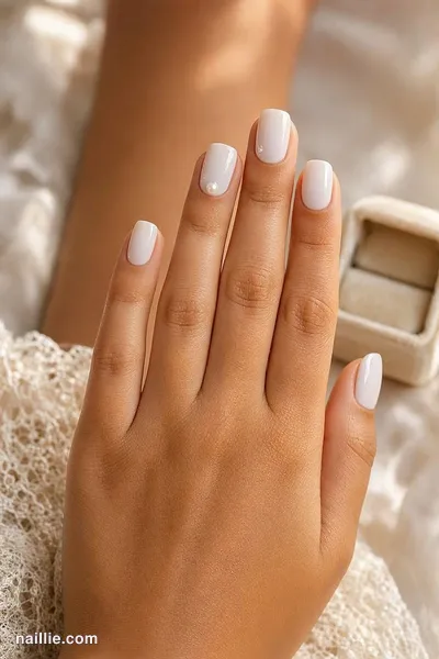 Close-up of short milky white glossy nails on ivory lace next to a ring box