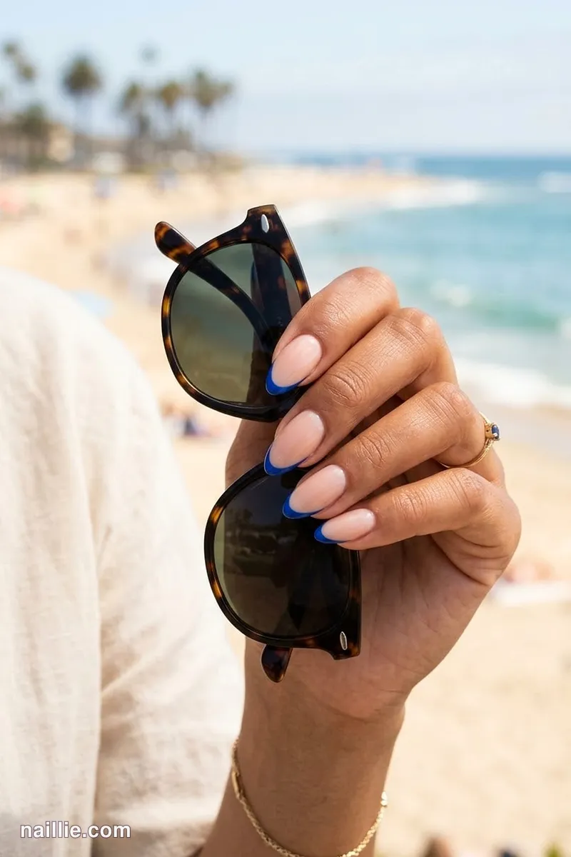 Close-up of almond nails with cobalt blue French tips over a sheer nude base