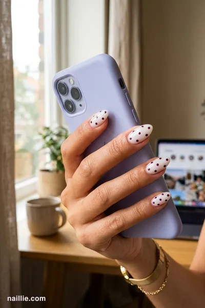 Close-up of almond nails with playful deep plum polka dots