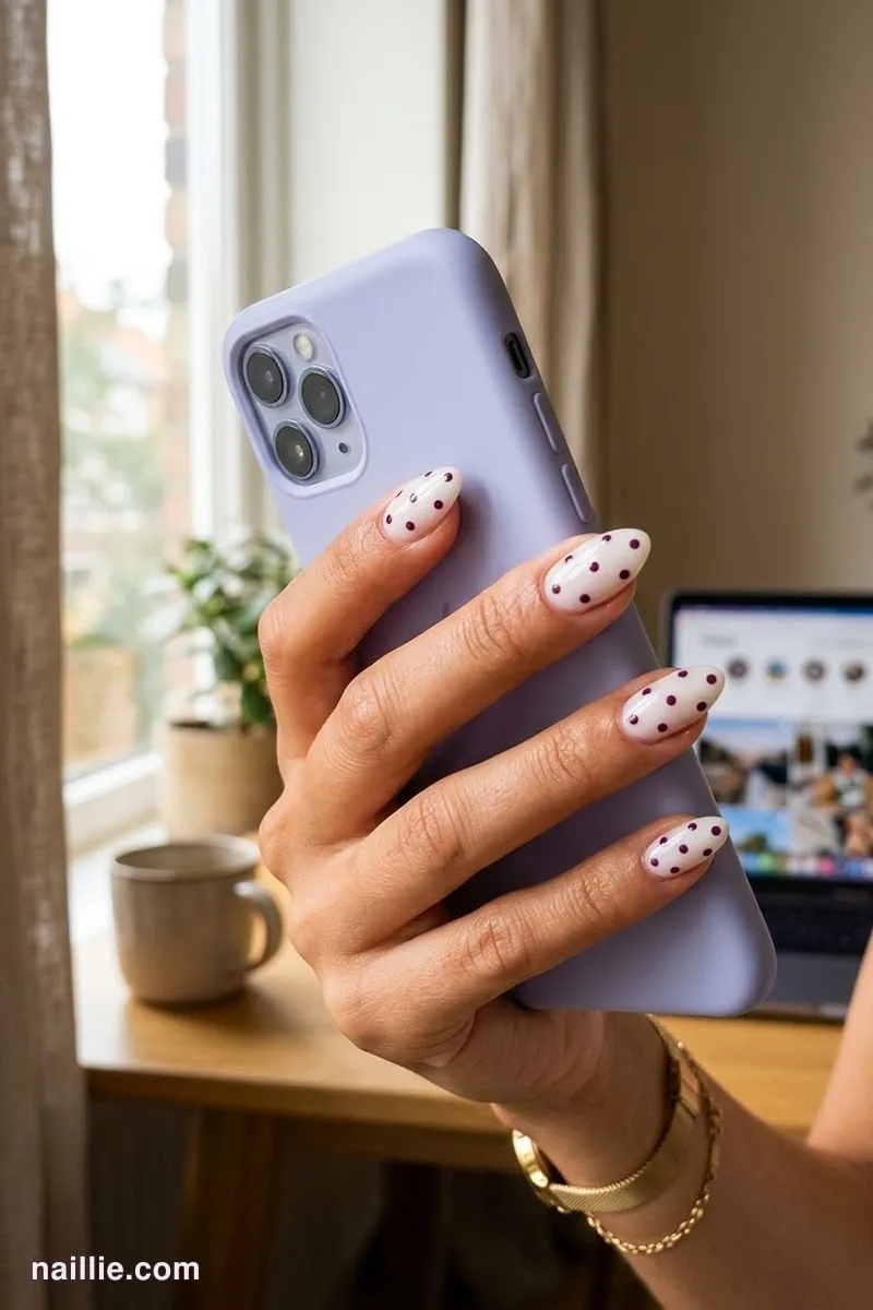 Close-up of almond nails with playful deep plum polka dots