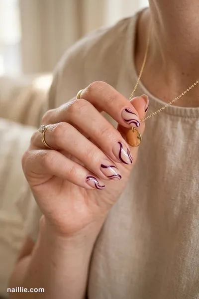 Close-up of oval nails with deep plum abstract swirls on a nude base