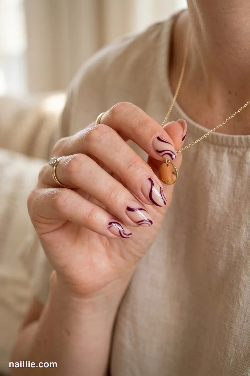Close-up of oval nails with deep plum abstract swirls on a nude base