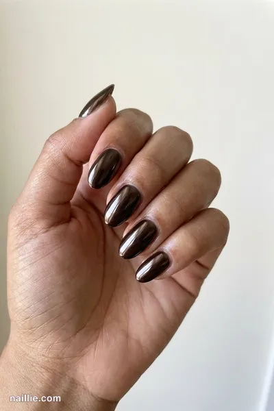 Close-up of oval nails with espresso brown polish and a mirror-like chrome finish — look 2