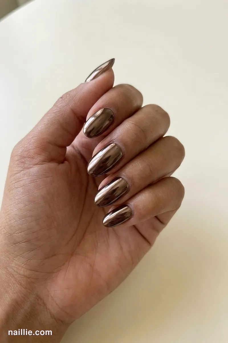Close-up of oval nails with espresso brown polish and a mirror-like chrome finish