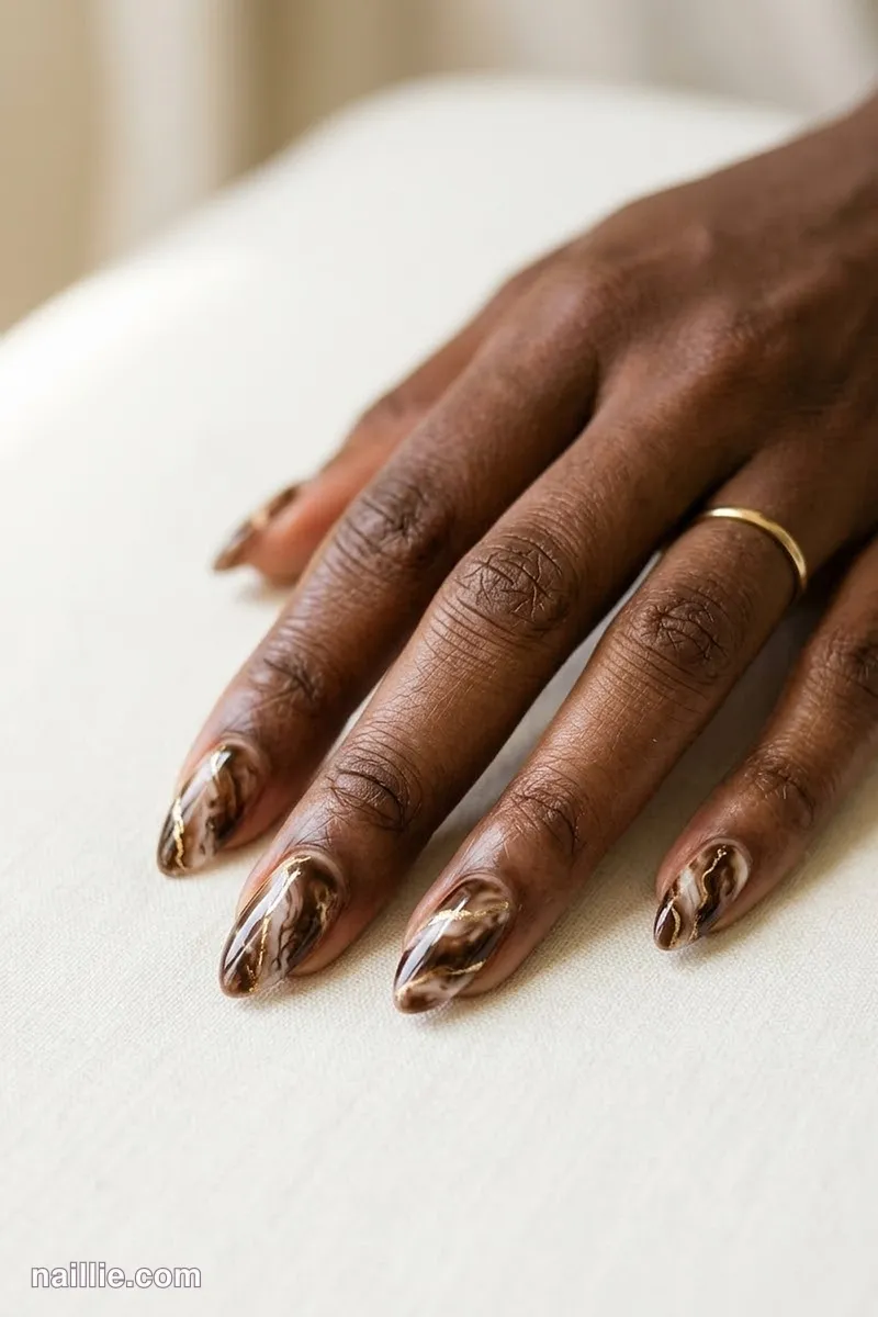 Close-up of almond nails with espresso brown marble swirls with gold veins