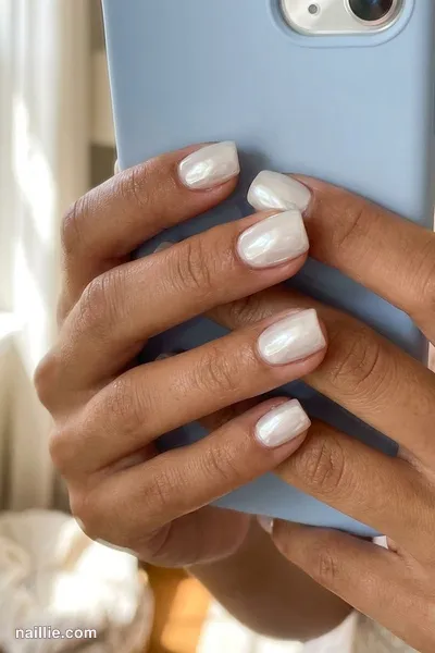 Close-up of short square nails with milky white polish and a mirror-like chrome finish