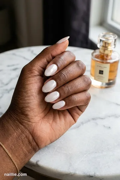 Close-up of short almond nails with milky white polish and a pearly glazed-donut shimmer