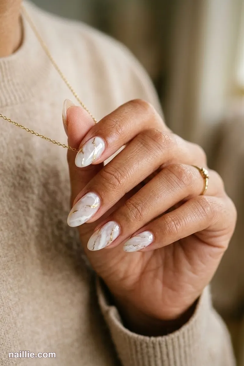 Close-up of almond nails with milky white marble swirls with gold veins