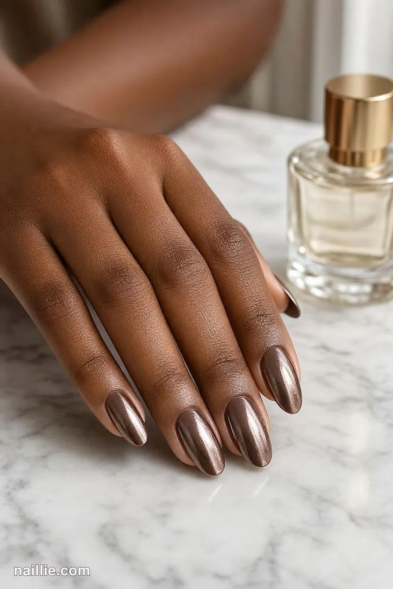 Close-up of almond nails with mocha polish and a mirror-like chrome finish