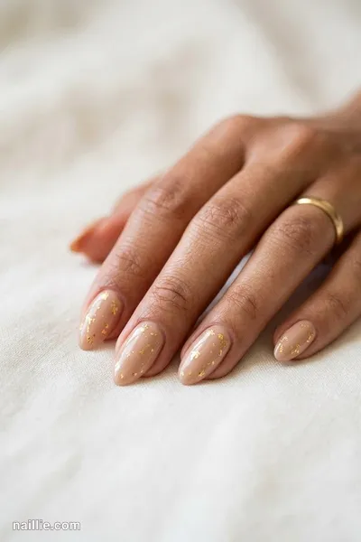 Close-up of almond nails with nude beige polish and delicate gold foil flakes