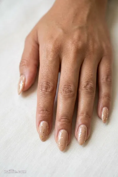 Close-up of almond nails with nude beige polish and delicate gold foil flakes — look 3