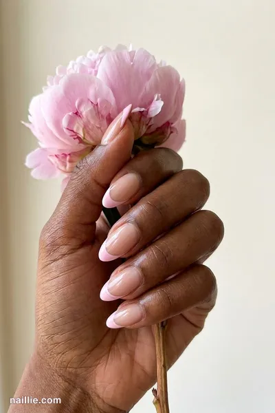 Close-up of almond nails with pastel pink French tips over a sheer nude base