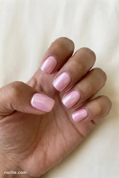 Close-up of short square nails with pastel pink polish and a pearly glazed-donut shimmer