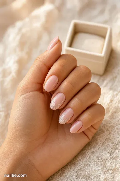 Close-up of soft pink nude nails with one sparkly glitter accent nail next to a ring box — look 2