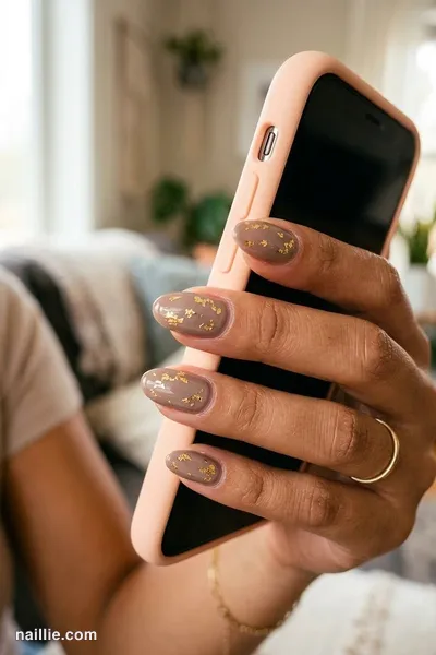 Close-up of oval nails with taupe polish and delicate gold foil flakes — look 2