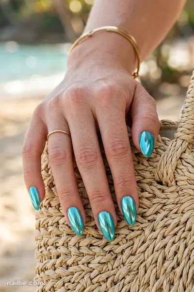 Close-up of almond nails with turquoise polish and a mirror-like chrome finish