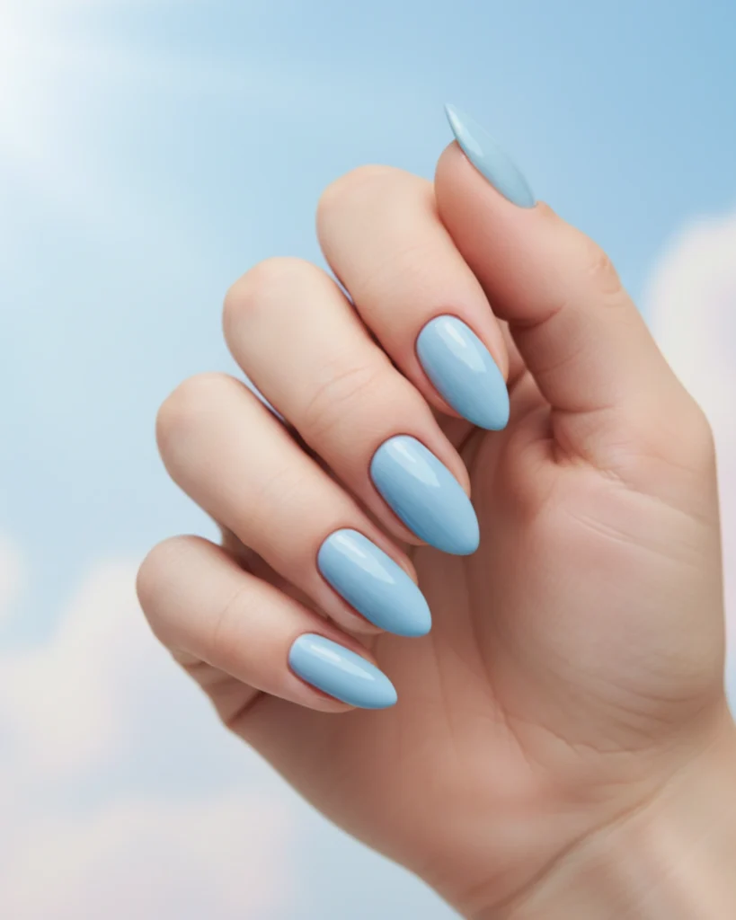 A close-up of a hand with long, almond-shaped nails painted in a glossy, solid sky blue polish against a sky background.
